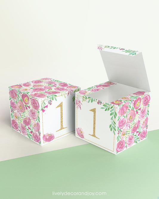 Paper cube shown as a closed block and also as an open box. It has pink floral designs and the number 1 in gold.