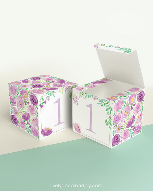 Paper cube shown as a closed block and also as an open box. It has purple floral designs and the number 1 in lavender.