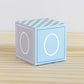 Paper building block in tints of blue and light grey. It has the number 0 on the sides and is on a wood table or shelf.