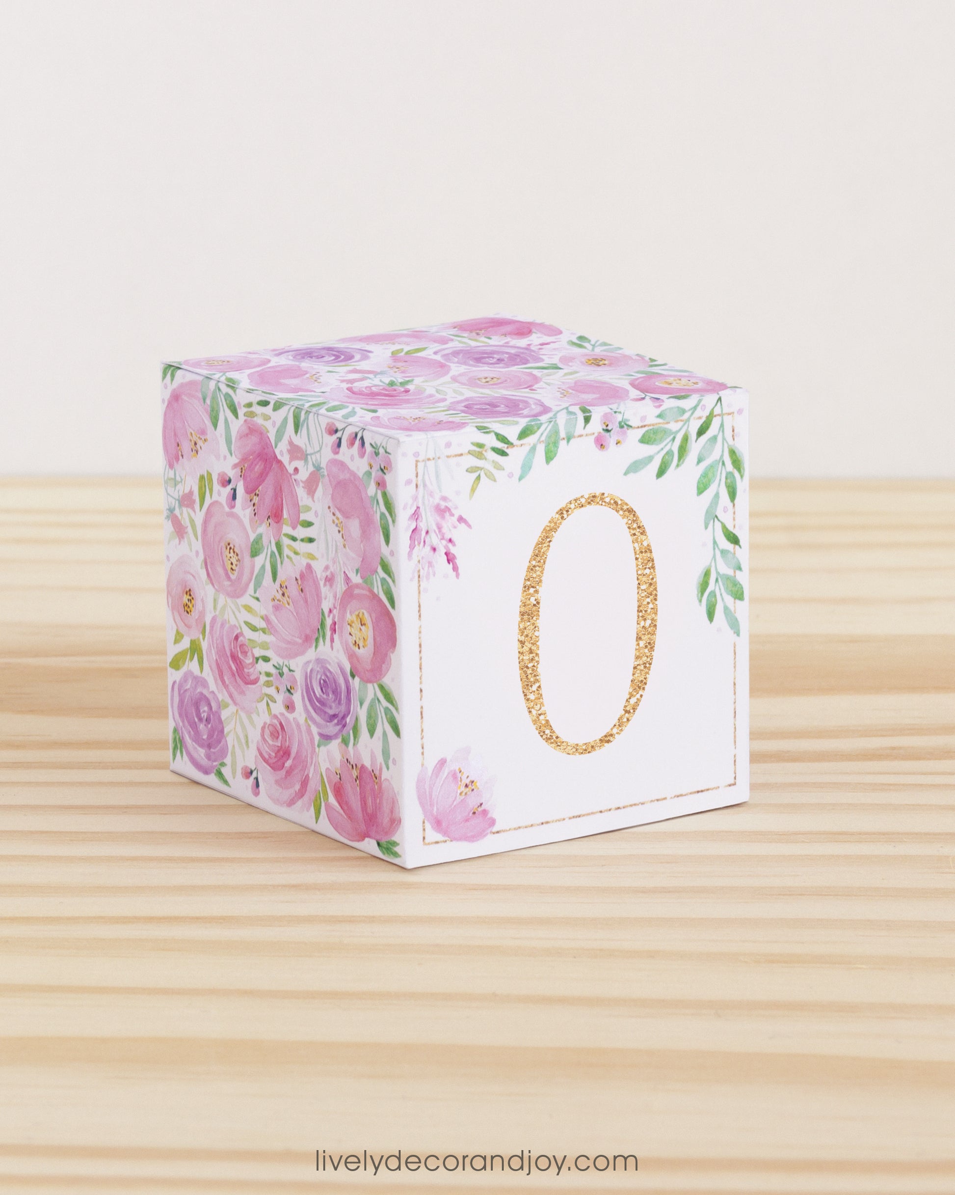 Paper building block with blush flowers, green leaves, and the digit 0 in peach. It is on a wooden table or shelf.