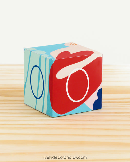 Paper building block in coral reef colors. It has the number 0 on the sides and is on a wood table or shelf.