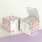 Paper cube shown as a closed block and also as an open box. Has blush and lavender floral designs and the number 1 in peach.