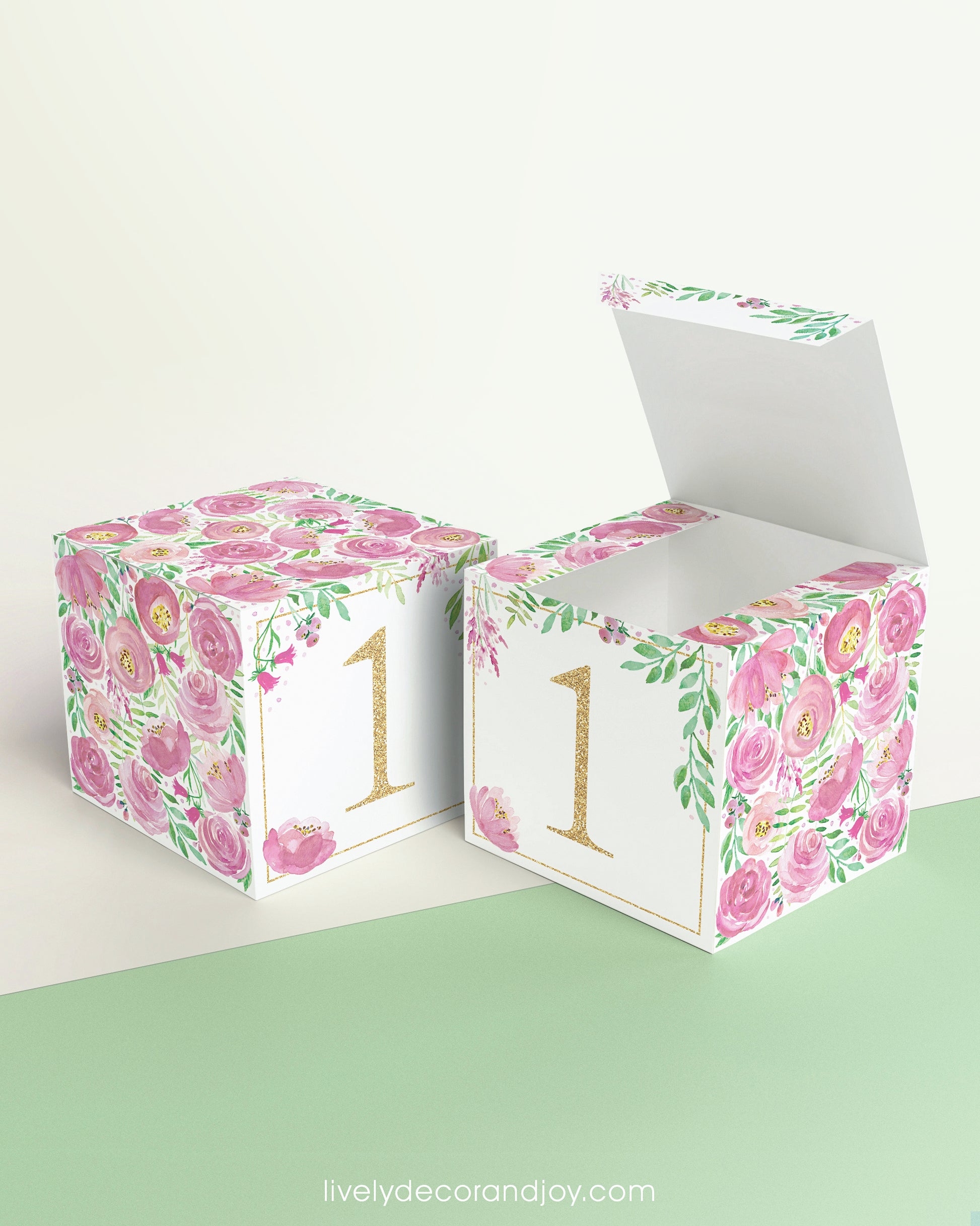 Paper cube shown as a closed block and also as an open box. It has pink floral designs and the number 1 in gold.