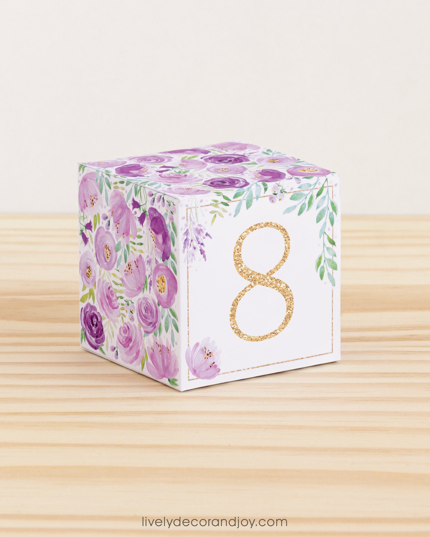 Baby block with purple and pink flowers and the digit 8 in a gold glitter-like pattern on the front.