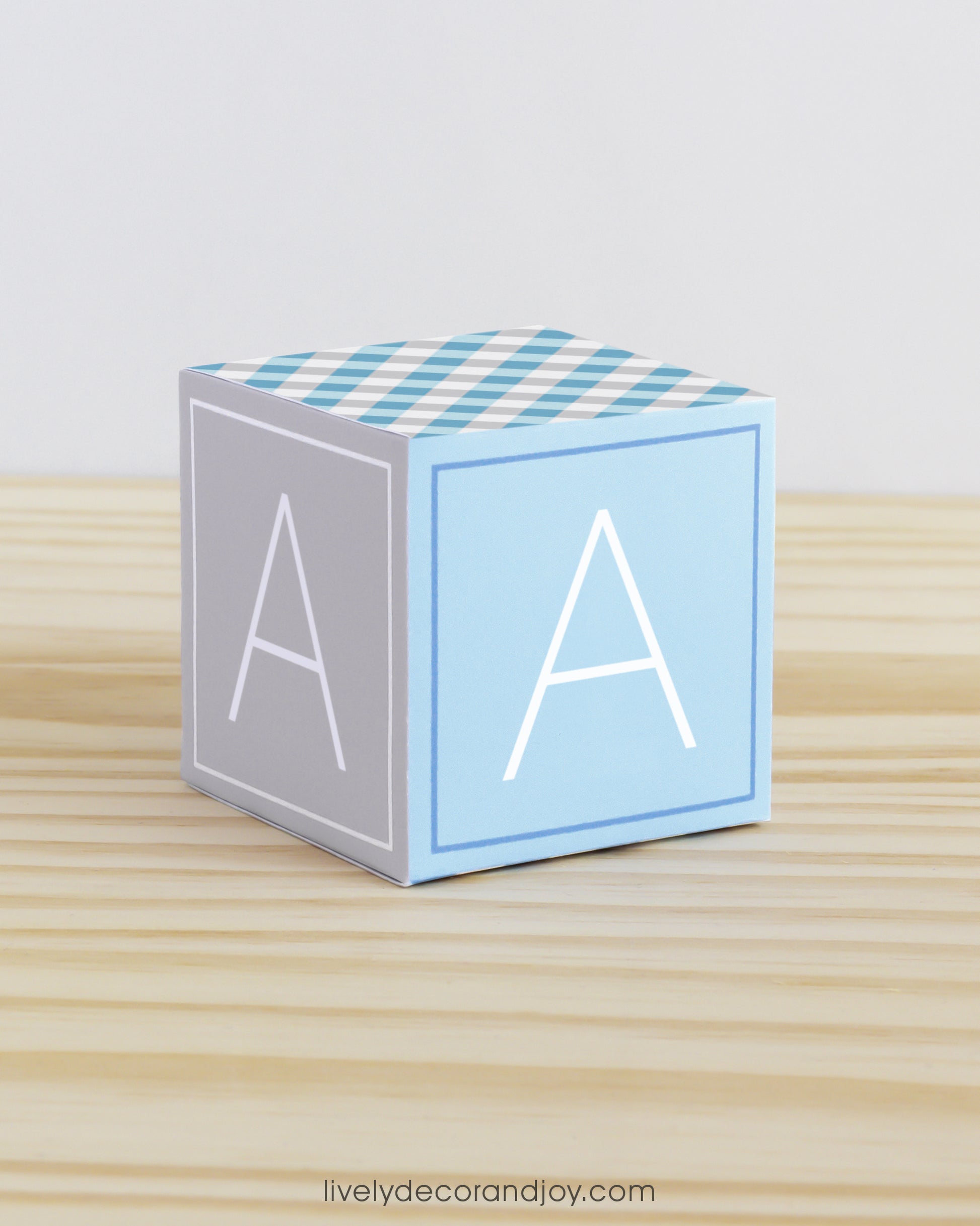 Large DIY building block with the letter A in tints of blue and light grey.The paper cube is on a wooden table.