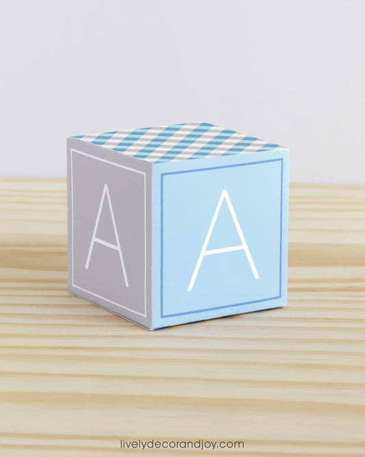 Large DIY building block with the letter A in tints of blue and light grey.The paper cube is on a wooden table.