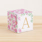 Large DIY block with the letter A in gold and floral designs in pink and green.The paper cube is on a wooden table.