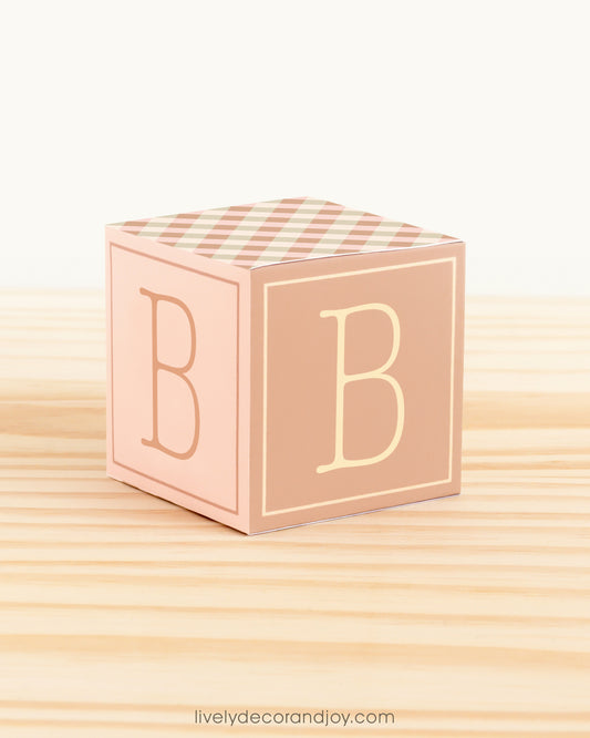 On a wooden table is a paper alphabet block in cottagecore colors with the letter B on the sides.