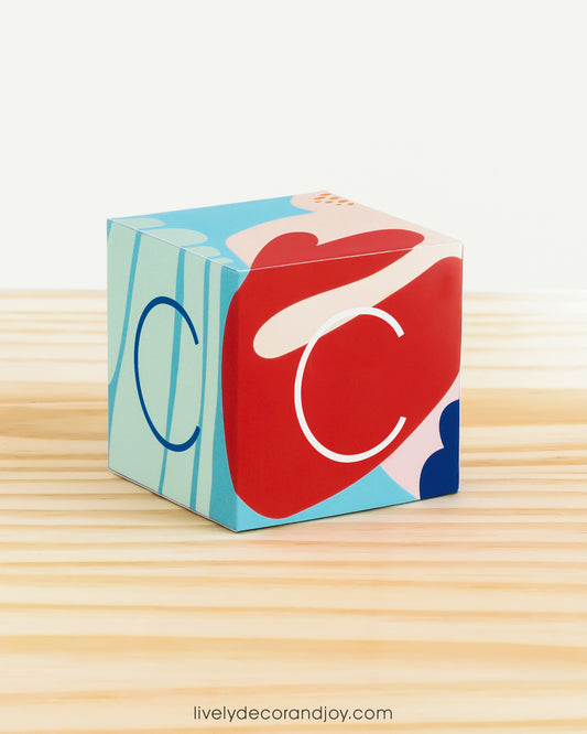 A paper cube in coral reef colors with the letter C on the sides. Features an abstract, modern design.