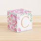 A paper cube with boho designs on a wooden surface. On the front, it has a capital C and a thin square frame in gold.
