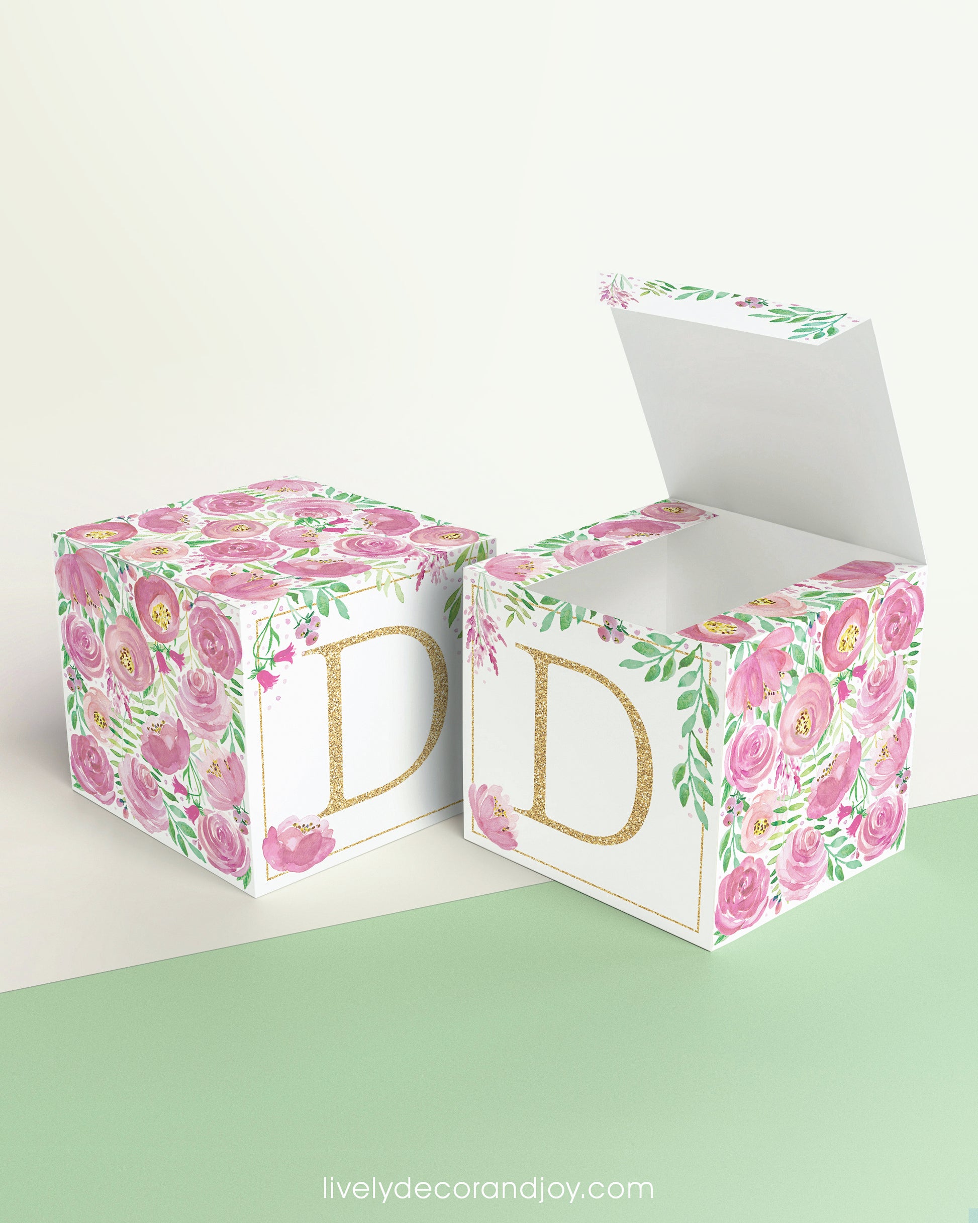 Two paper cubes with pink floral designs and the letter D in gold. One has the top open, showing it can be a cube or a box.