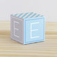 Baby block in tints of blue and light grey. Has the letter E on the sides. Made of paper.