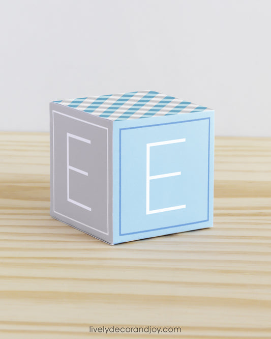 Baby block in tints of blue and light grey. Has the letter E on the sides. Made of paper.