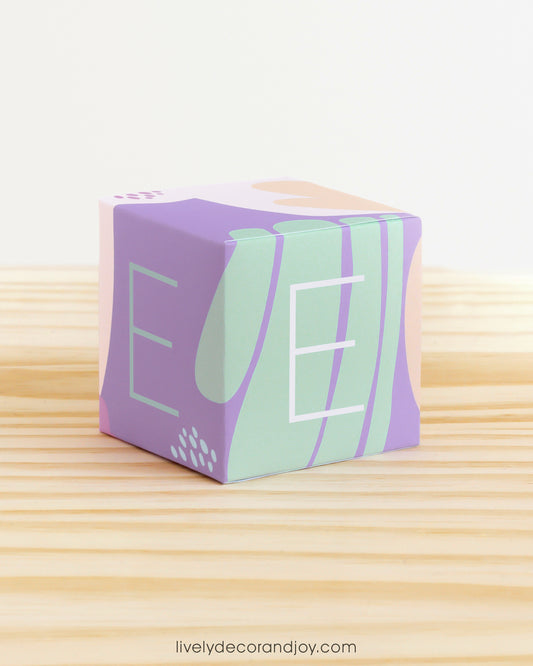 Baby block in pastel colors. Has the letter E on the sides and organic designs. Made of paper.