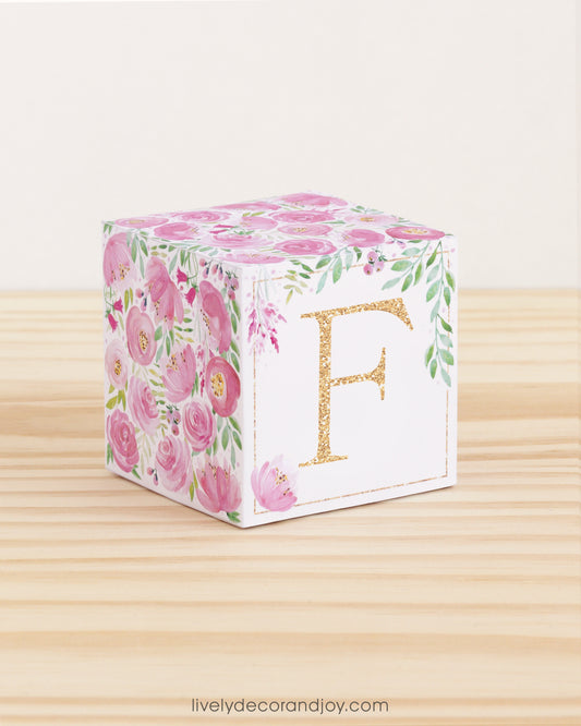 Paper building block features watercolor flowers and leaves in shades of pink and green. A gold capital F is on the front.