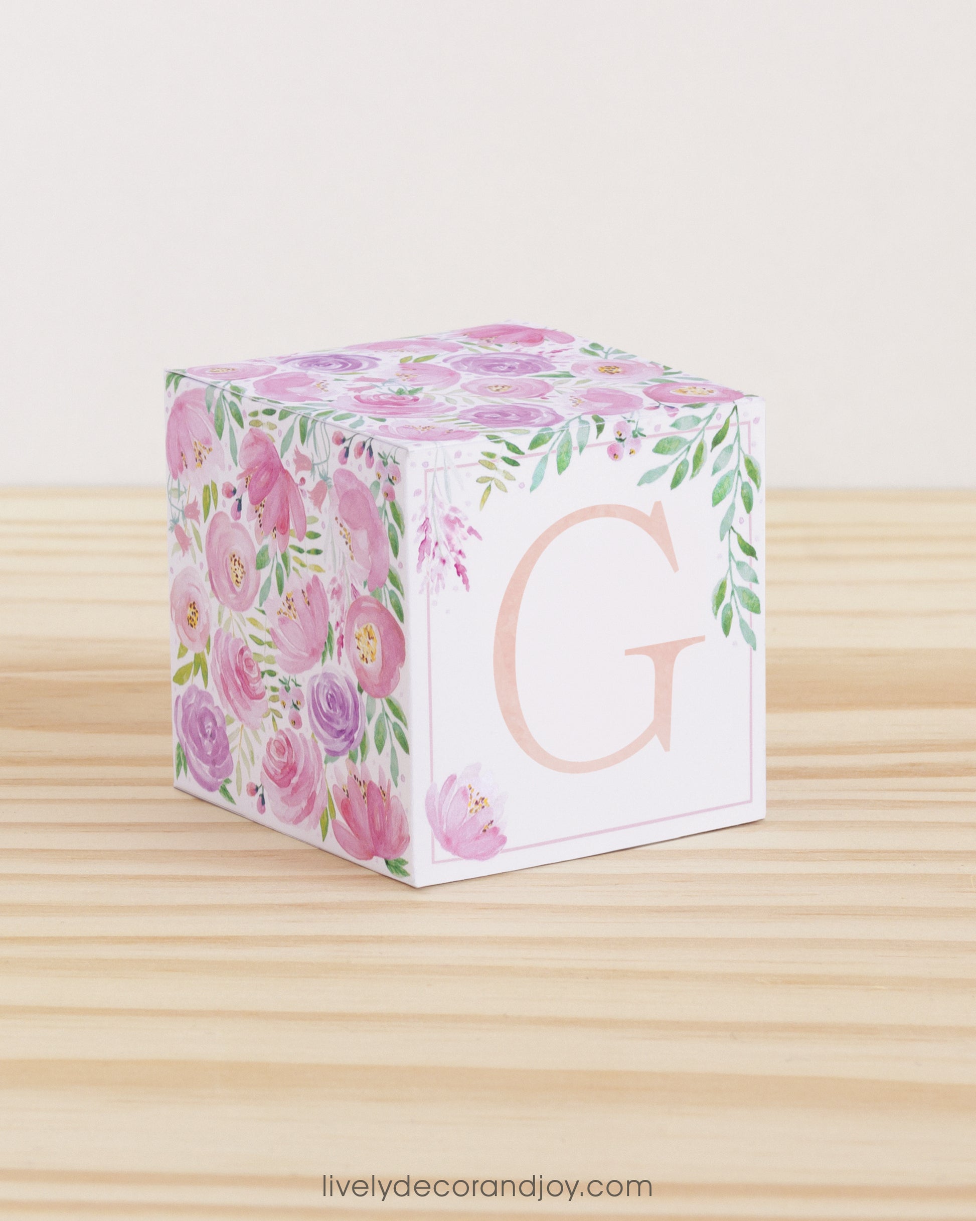 Letter block with printed blush and lavender floral designs and a peach capital G on the front. It is made of paper.