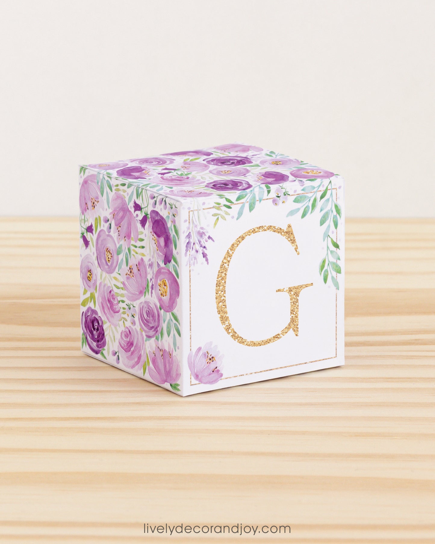 Letter block with printed purple and green floral designs and a gold capital G on the front. It is made of paper.