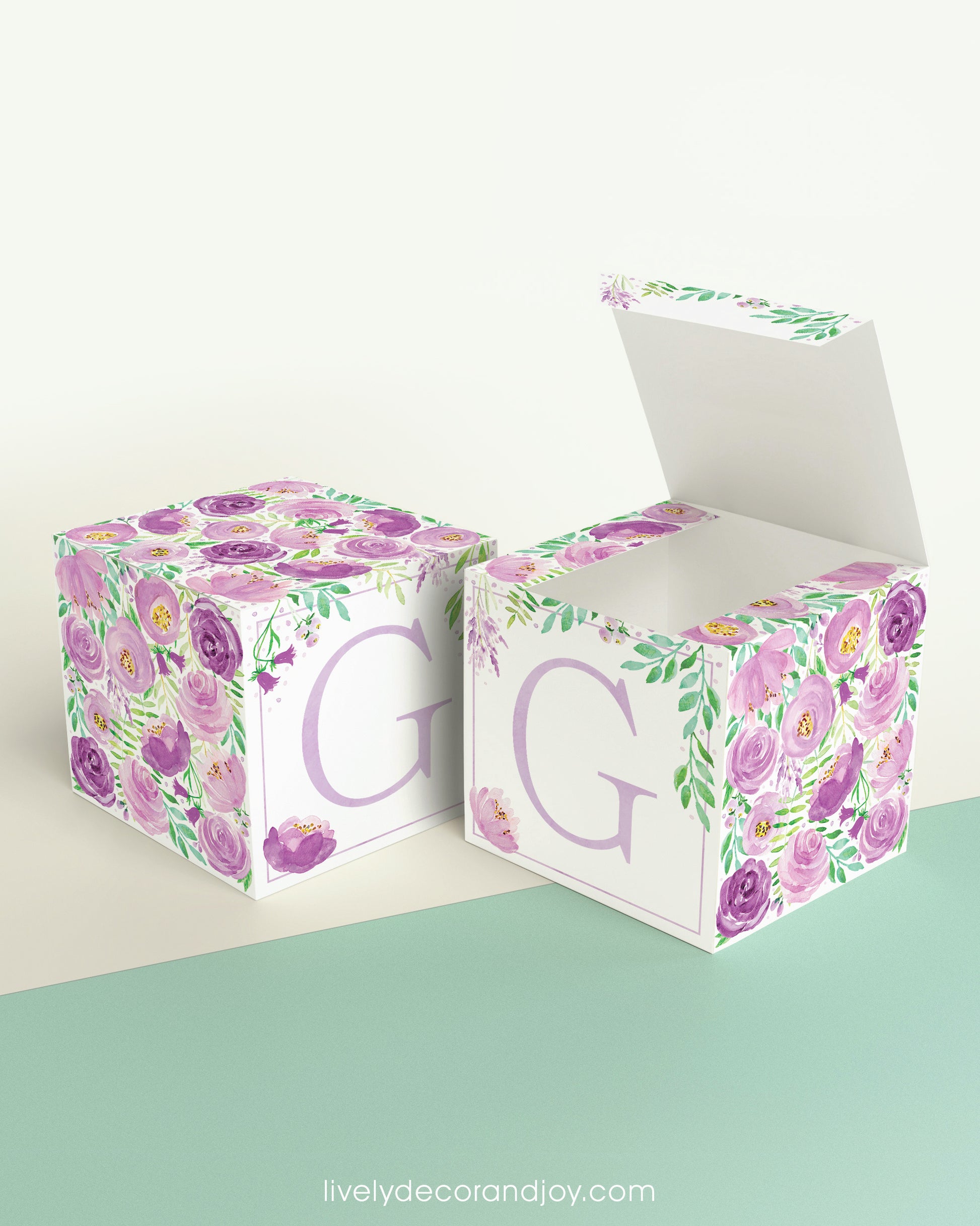 Two blocks made of paper, one has the top lid open. Floral designs cover all sides except the front, which has the letter G.