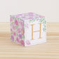 Paper cube with floral cottagecore motifs in blush and lavender. It has a peach capital H on the front.