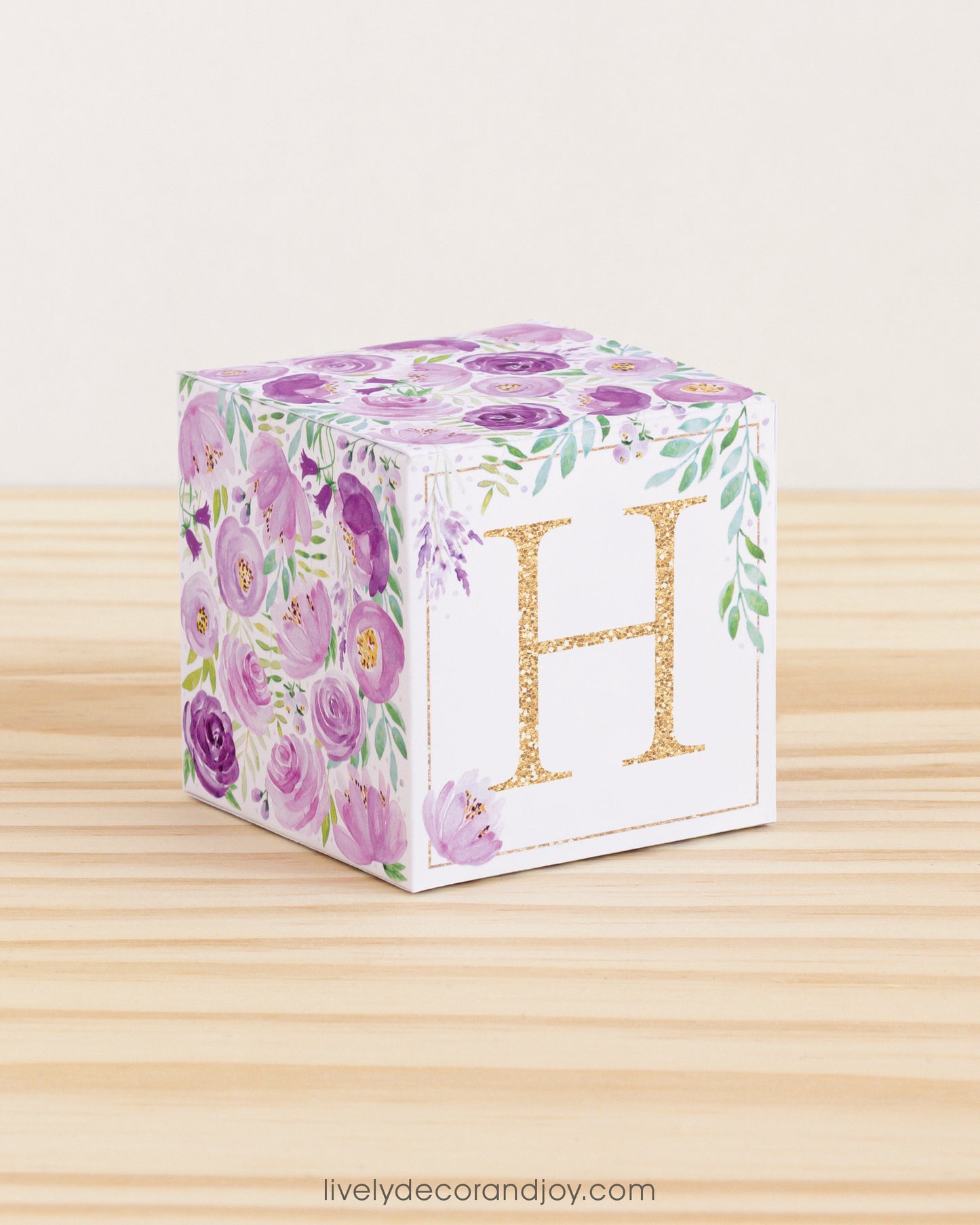 Paper cube with floral cottagecore motifs and a capital H on the front. It features purple and green flowers and leaves.