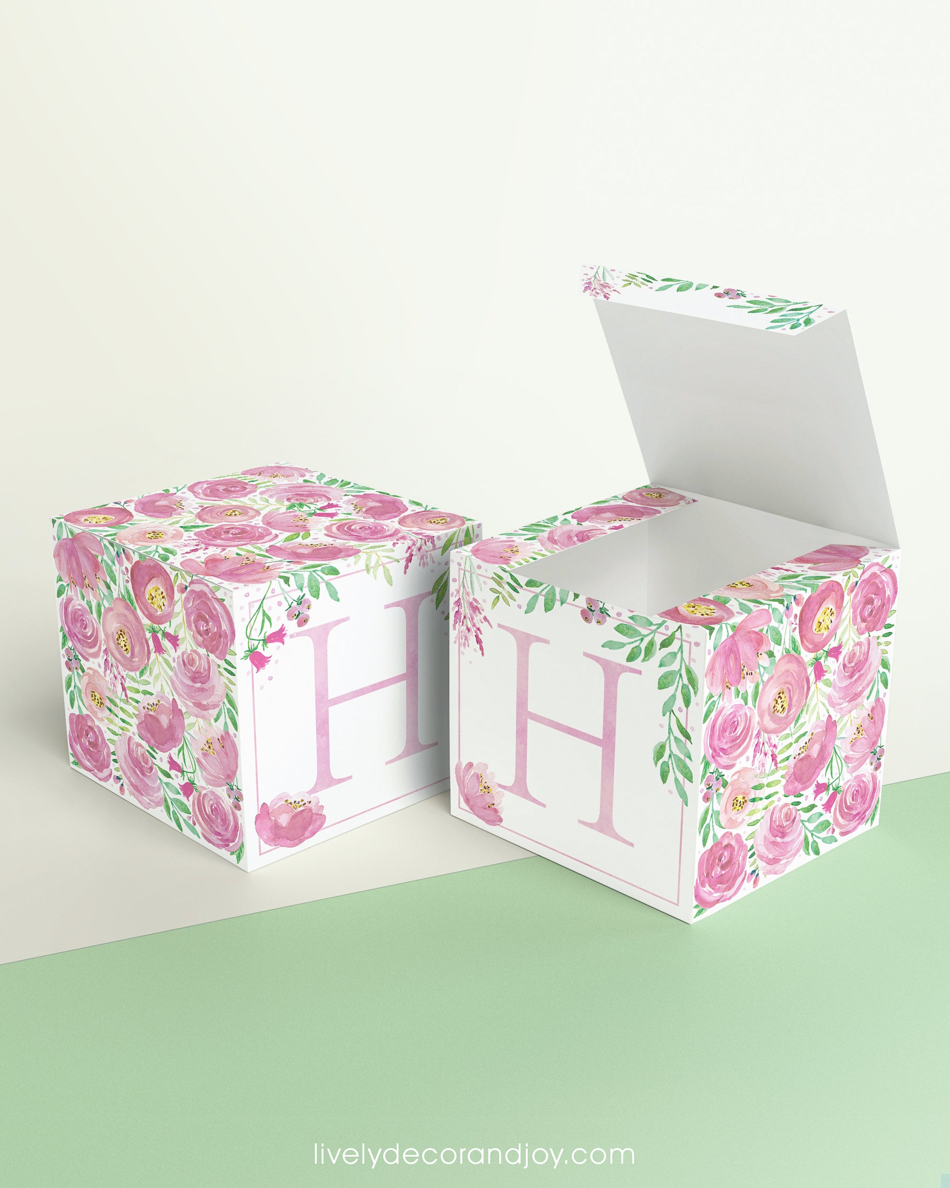 Two identical paper cubes with printed floral designs and the letter H. One has the top open, showing that it is a box.