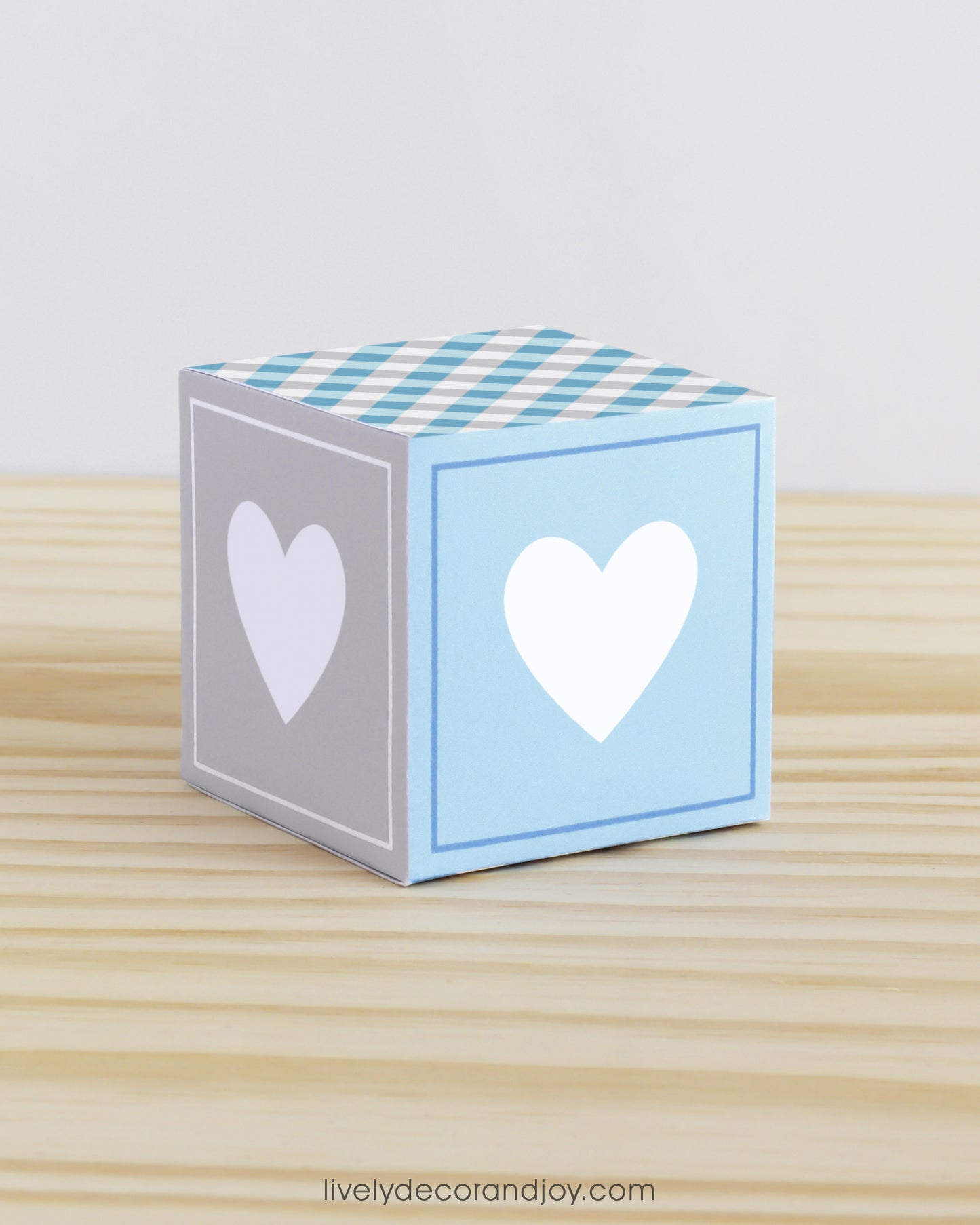 Paper alphabet cube with a heart on the sides. Designed in tints of blue and light grey. It is on a wooden table.