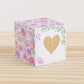 Paper cube with a big peach heart on the front and blush and lavender floral designs all around. It is on a wooden table.
