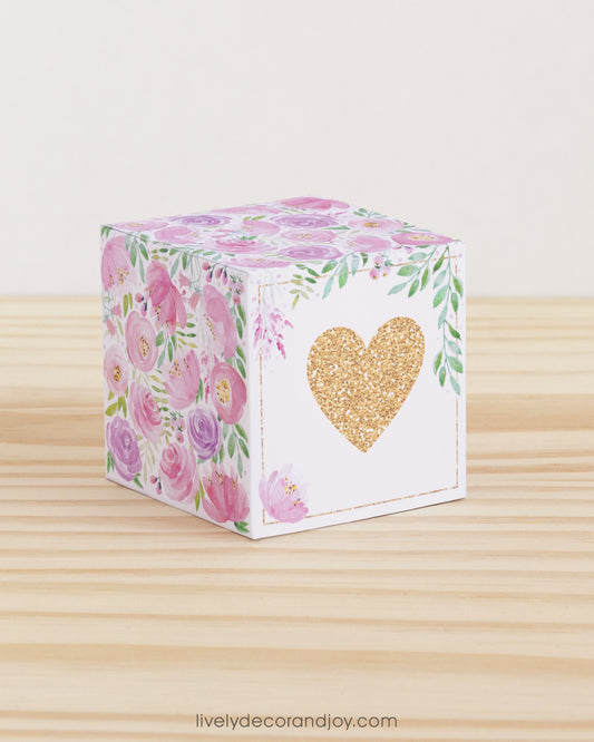 Paper cube with a big peach heart on the front and blush and lavender floral designs all around. It is on a wooden table.
