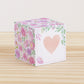 Paper cube with a big peach heart on the front and blush and lavender floral designs all around. It is on a wooden table.