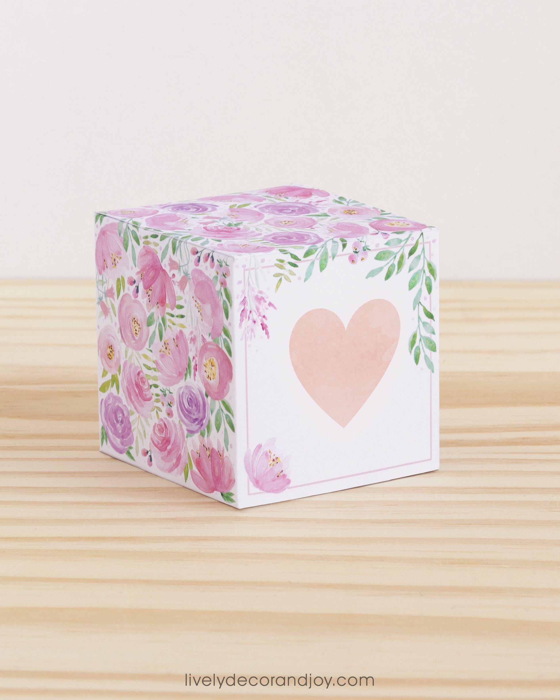 Paper cube with a big peach heart on the front and blush and lavender floral designs all around. It is on a wooden table.