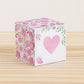 Paper cube with a big pink heart on the front and pink floral designs all around. It is on a wooden table.