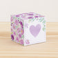 Paper cube with a big lavender heart on the front and purple floral designs all around. It is on a wooden table.