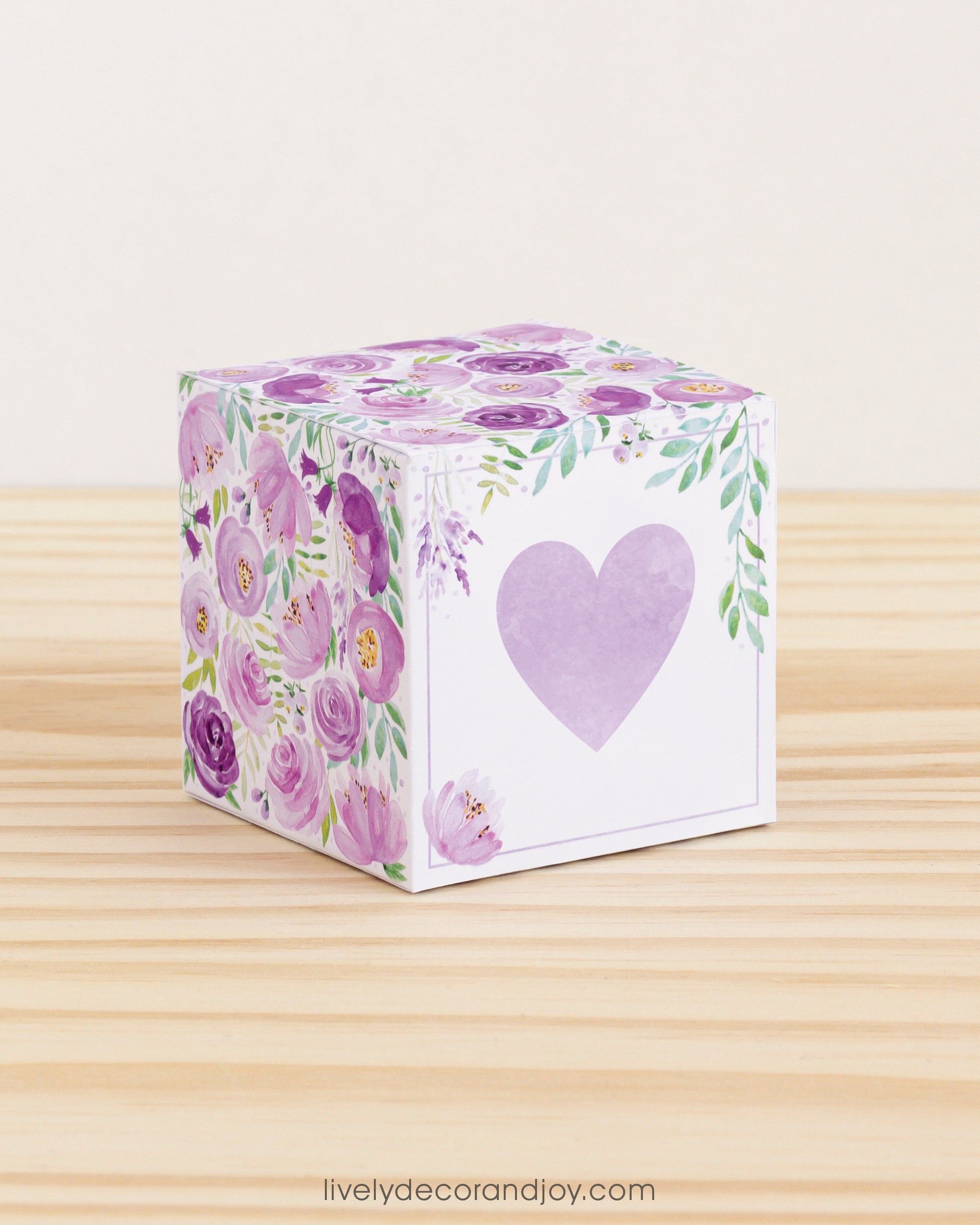 Paper cube with a big lavender heart on the front and purple floral designs all around. It is on a wooden table.