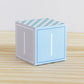 Building block made of printed paper and the letter I on the sides. It is on a wooden table.