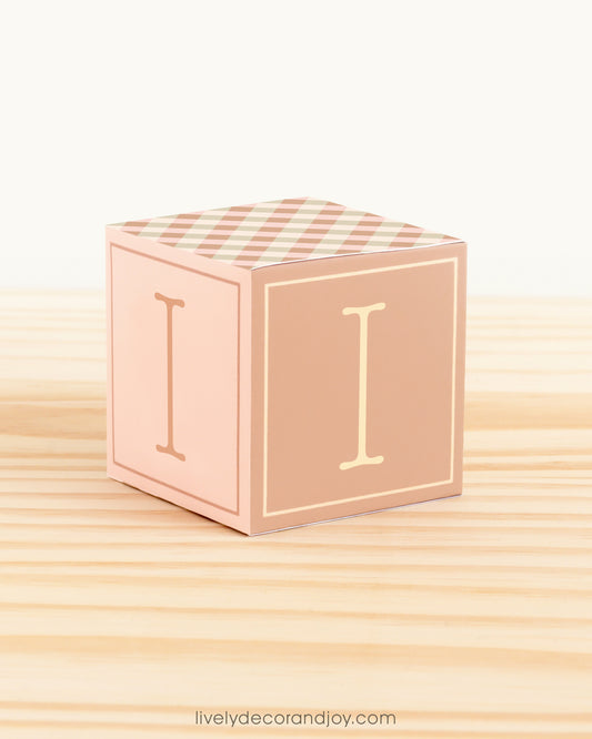 Building block made of printed paper and the letter I on the sides. Earthy tones. It is on a wooden table.