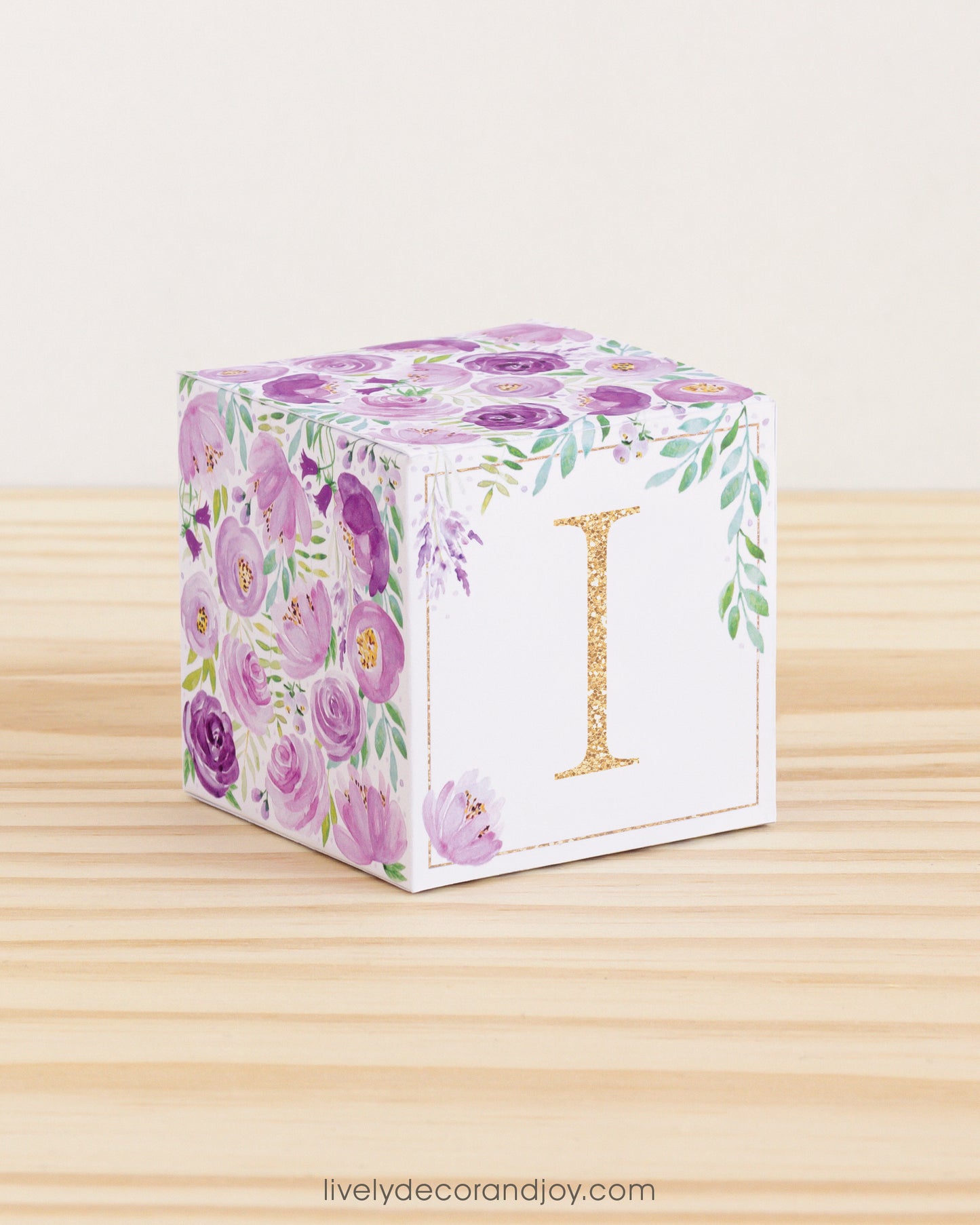 Building block made of printed paper with floral designs and the letter I on the front. It is on a wooden table.