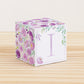 Building block made of printed paper with floral designs and the letter I on the front. It is on a wooden table.