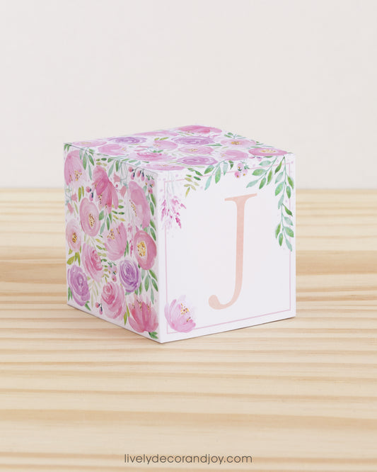 Block made of printed paper with watercolor flowers in blush and lavender. Has a peach letter J on the front.