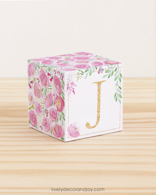 Block made of printed paper with watercolor flowers in pink tones and green leaves. Features a gold letter J on the front.