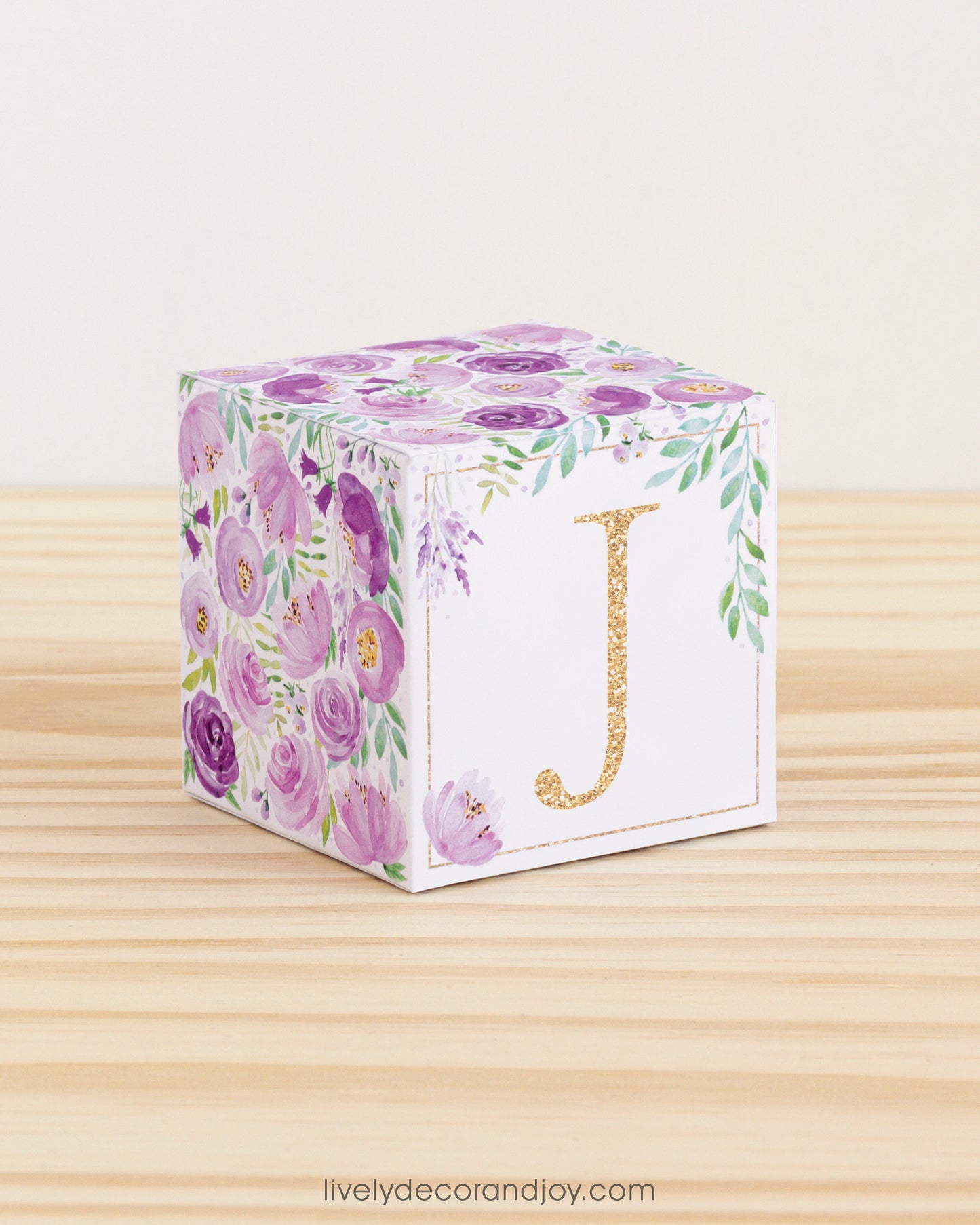 Block made of printed paper with watercolor flowers in purple tones and green leaves. Features a gold letter J on the front.