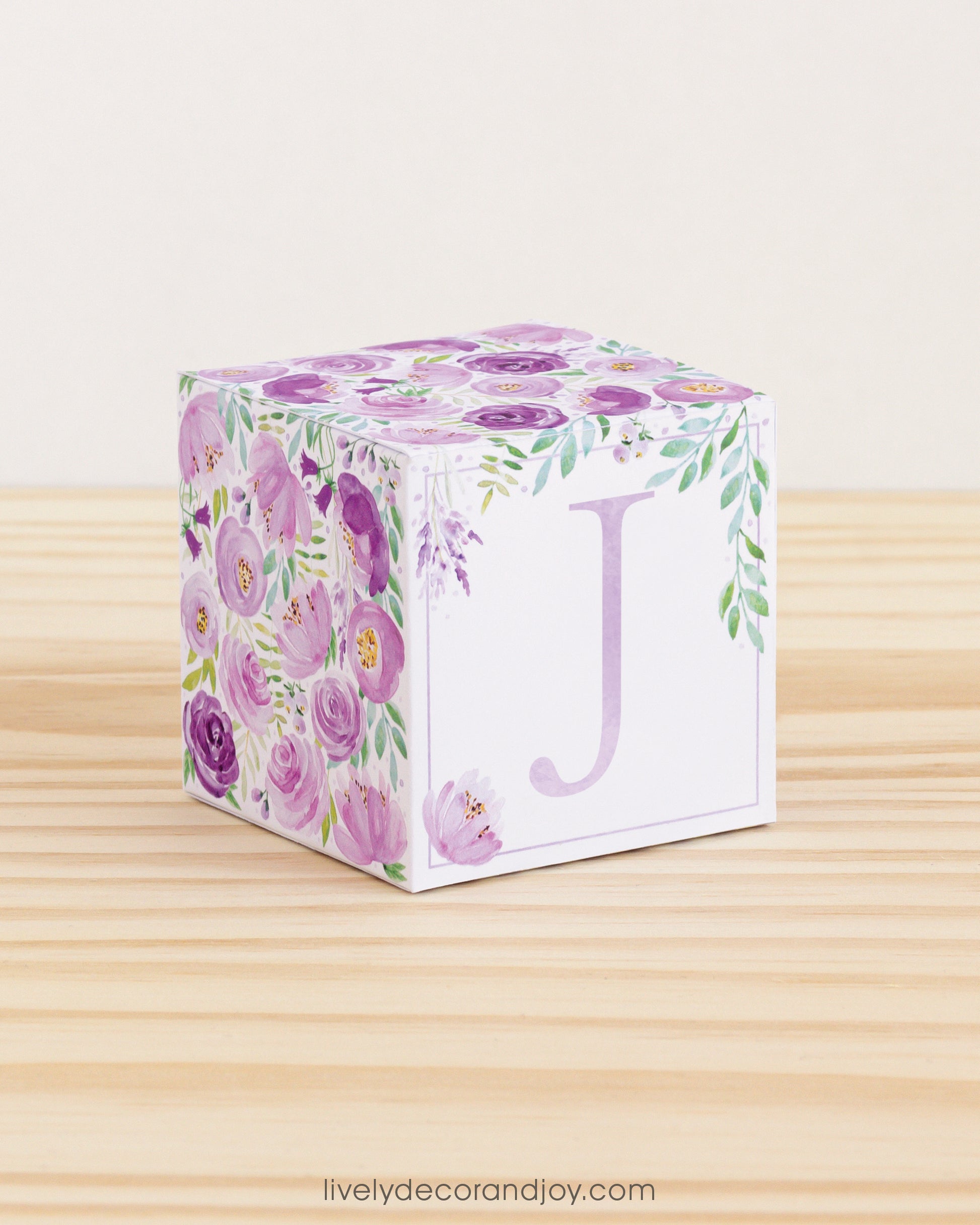 Block made of printed paper with watercolor flowers in purple tones and green leaves. Has a violet letter J on the front.