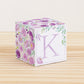 Big DIY block with the letter K in lavender and floral designs in purple and green.The paper cube is on a wooden table.