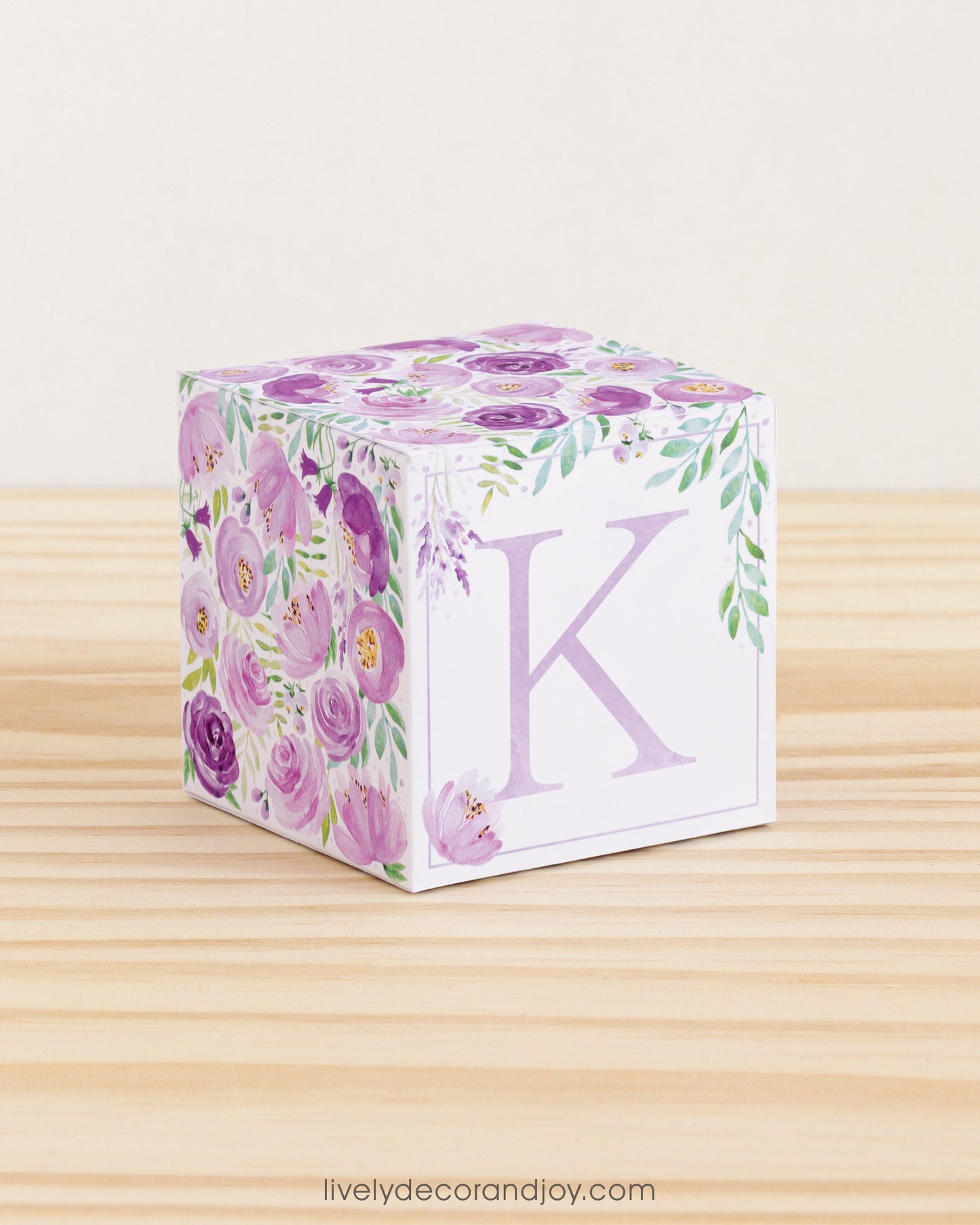 Big DIY block with the letter K in lavender and floral designs in purple and green.The paper cube is on a wooden table.