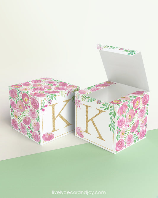Two paper cubes with the same floral design and a capital K on the front. One has the lid open showing it can also be a box.