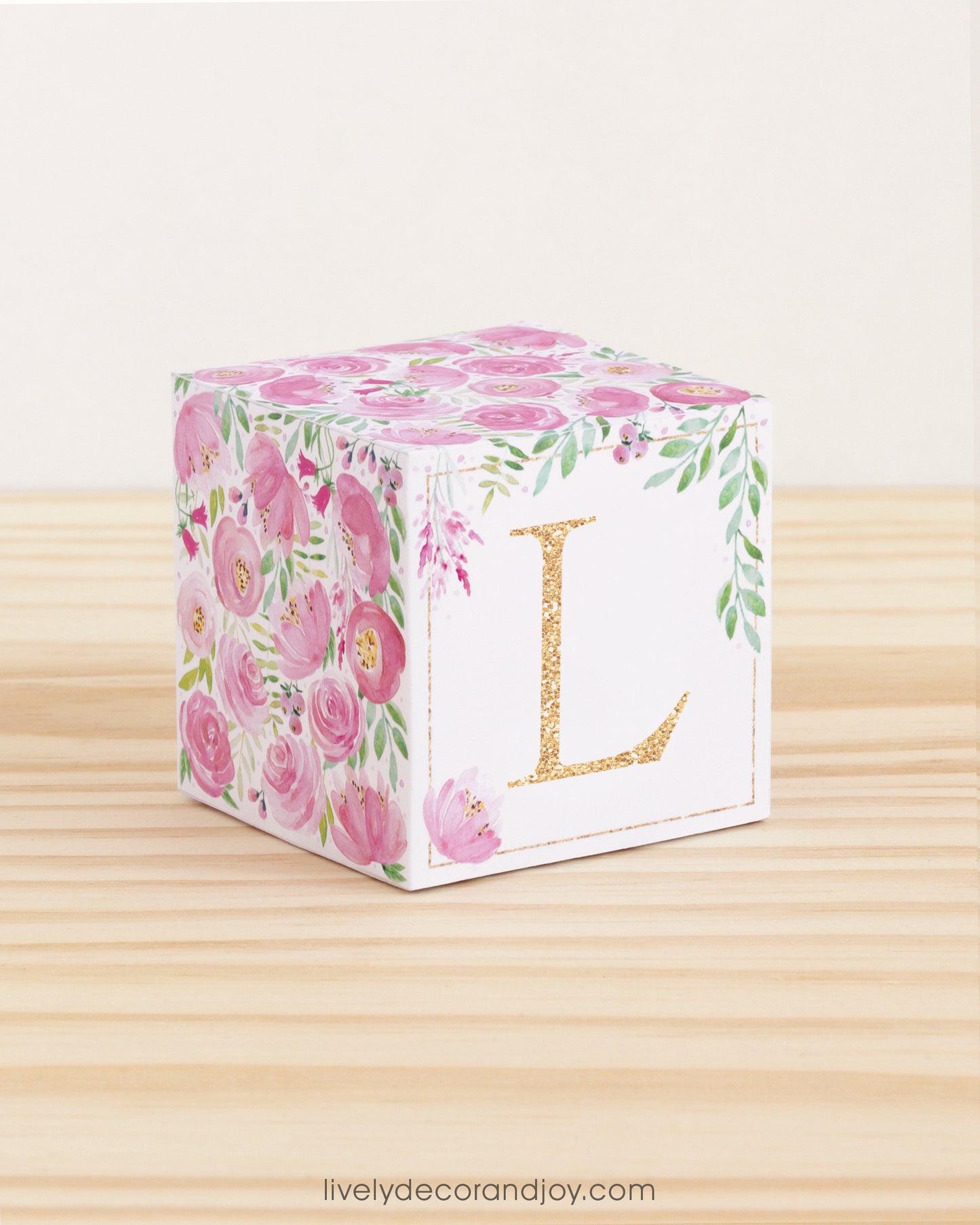 Cube with pink watercolor flowers and green leaves all around but only some on the front, where it has the letter L in gold.