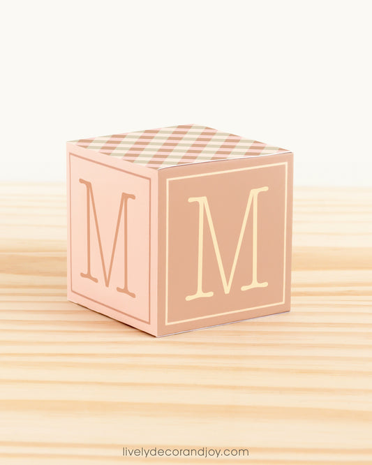 5 minute craft, ABC block on a wooden surface. Made of paper. On the sides, it has the capital M.