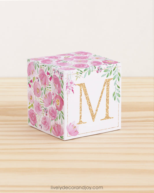 5 minute craft cube with floral designs on a wooden surface. On the front, it has a capital M and a square frame in gold.