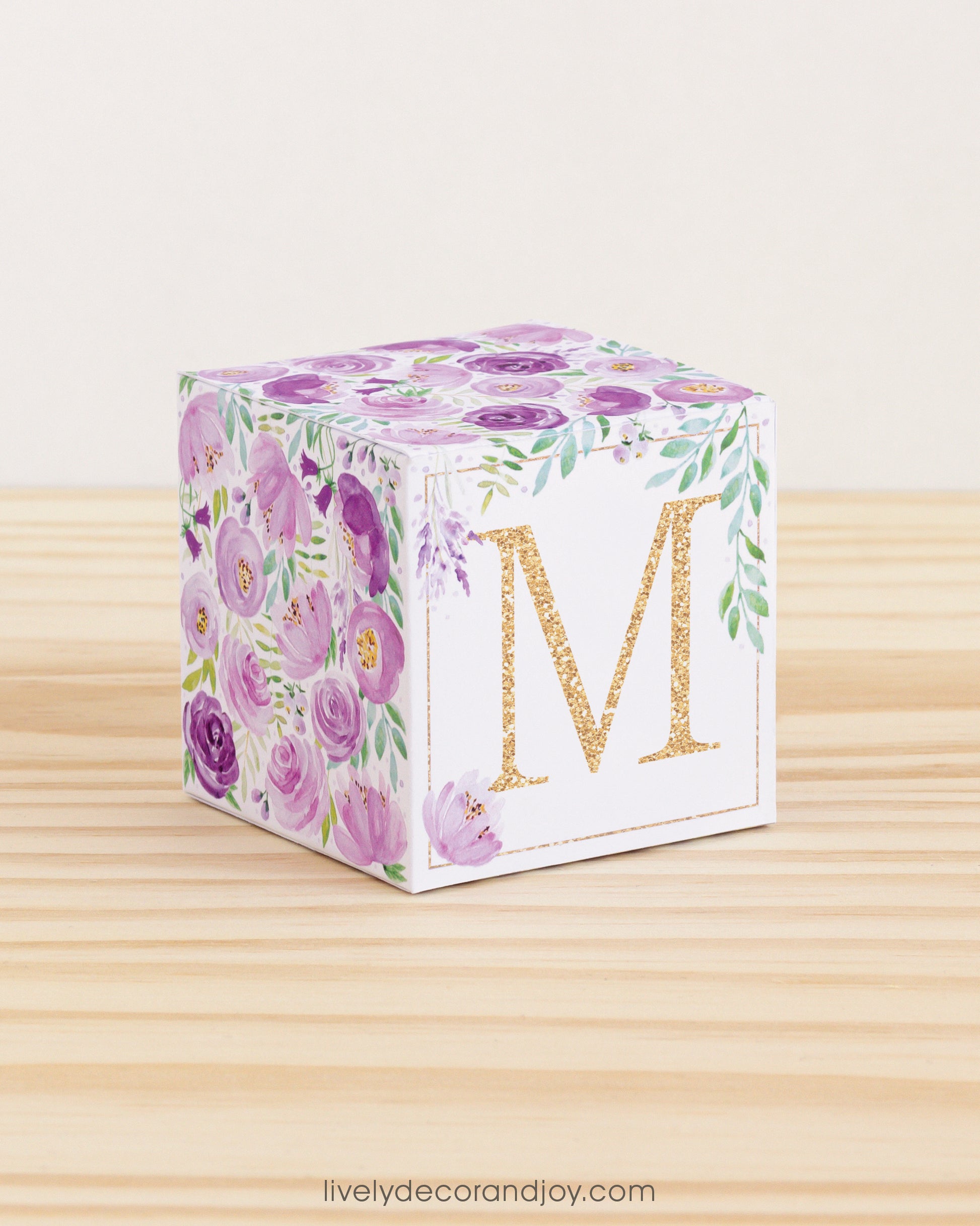 5 minute craft cube with floral designs on a wooden surface. On the front, it has a capital M and a square frame in gold.