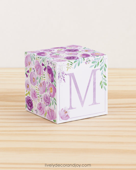 5 minute craft cube with floral designs on a wooden surface. On the front, it has a capital M and a square frame in lavender.