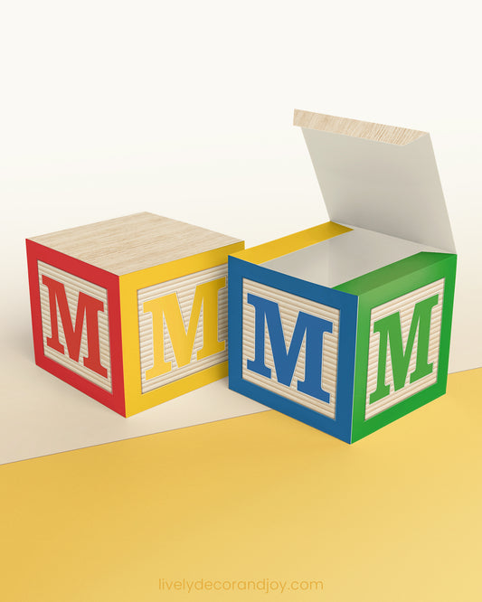 5 minute craft, ABC block on a wooden surface. Made of paper. On the sides, it has the capital M.